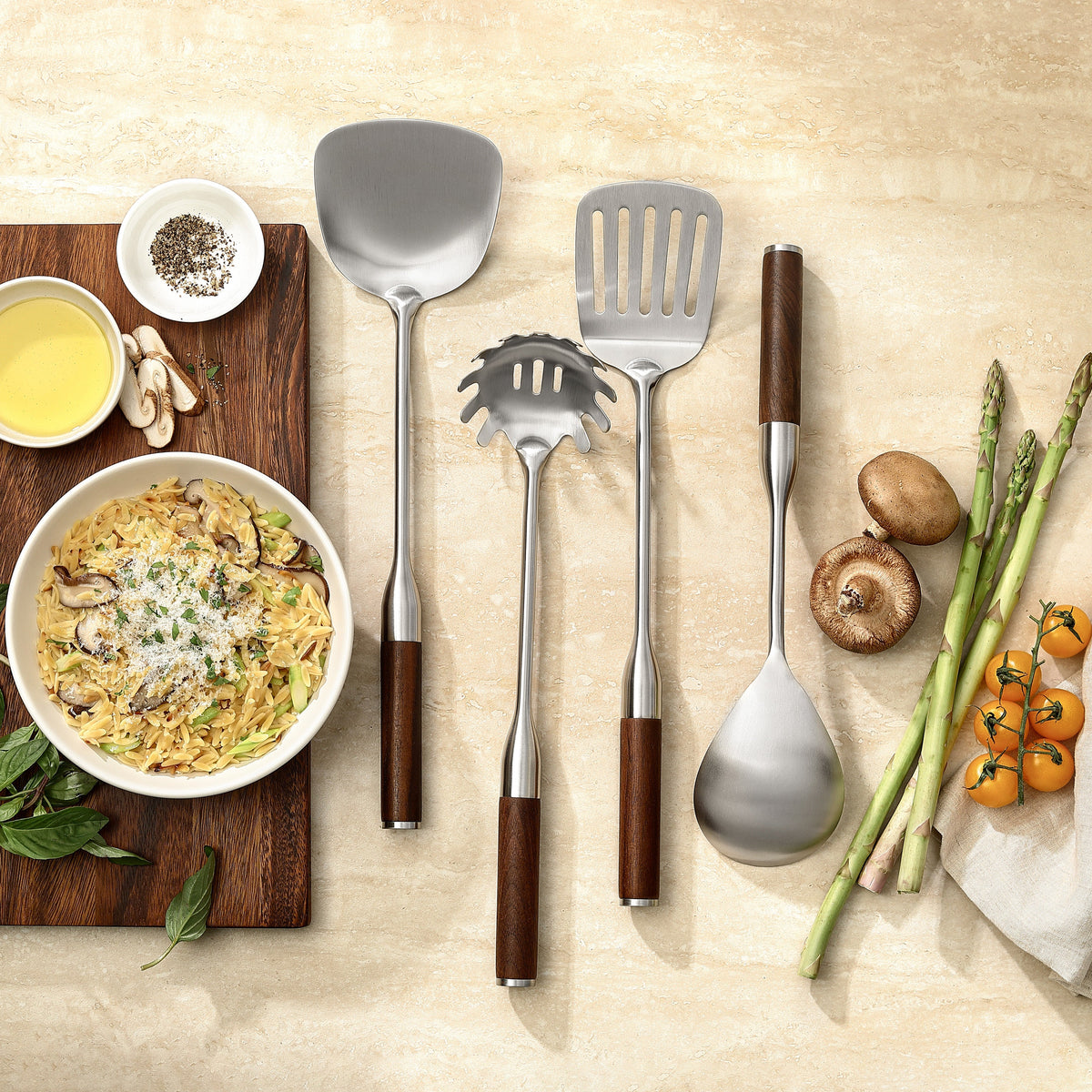 Die vier Küchenhelfer des Sets mit Griffen aus Walnuss neben einer Schüssel Pasta mit Pilzen und Parmesan