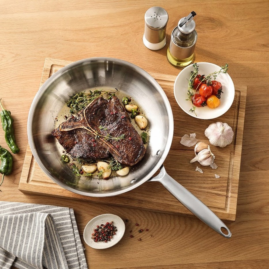 T-Bone-Steak mit Knoblauch in einer Bratpfanne 3-ply Edelstahl auf einem Schneidebrett