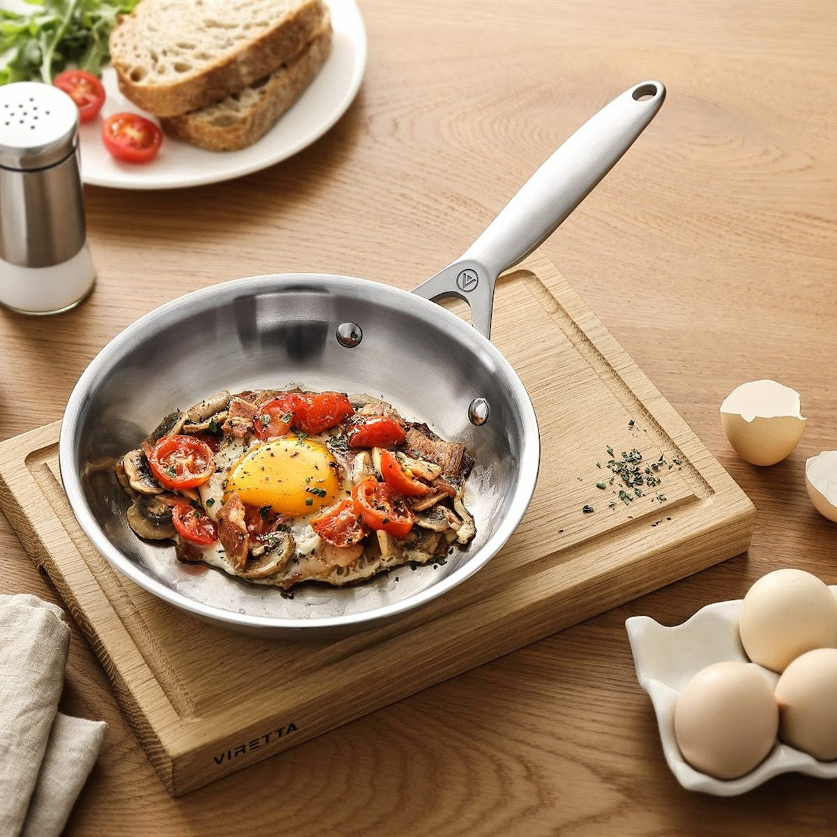 Spiegelei mit Tomaten und Pilzen in einer Bratpfanne 3-ply Edelstahl auf einem Schneidebrett