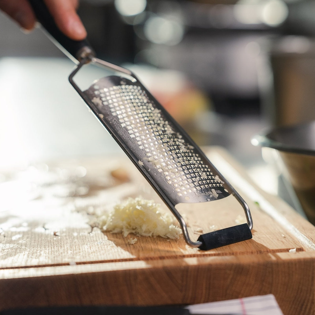 Feine Reibe mit Griff aus G-10 auf einem Schneidebrett neben frisch geriebenem Knoblauch #Material_G-10