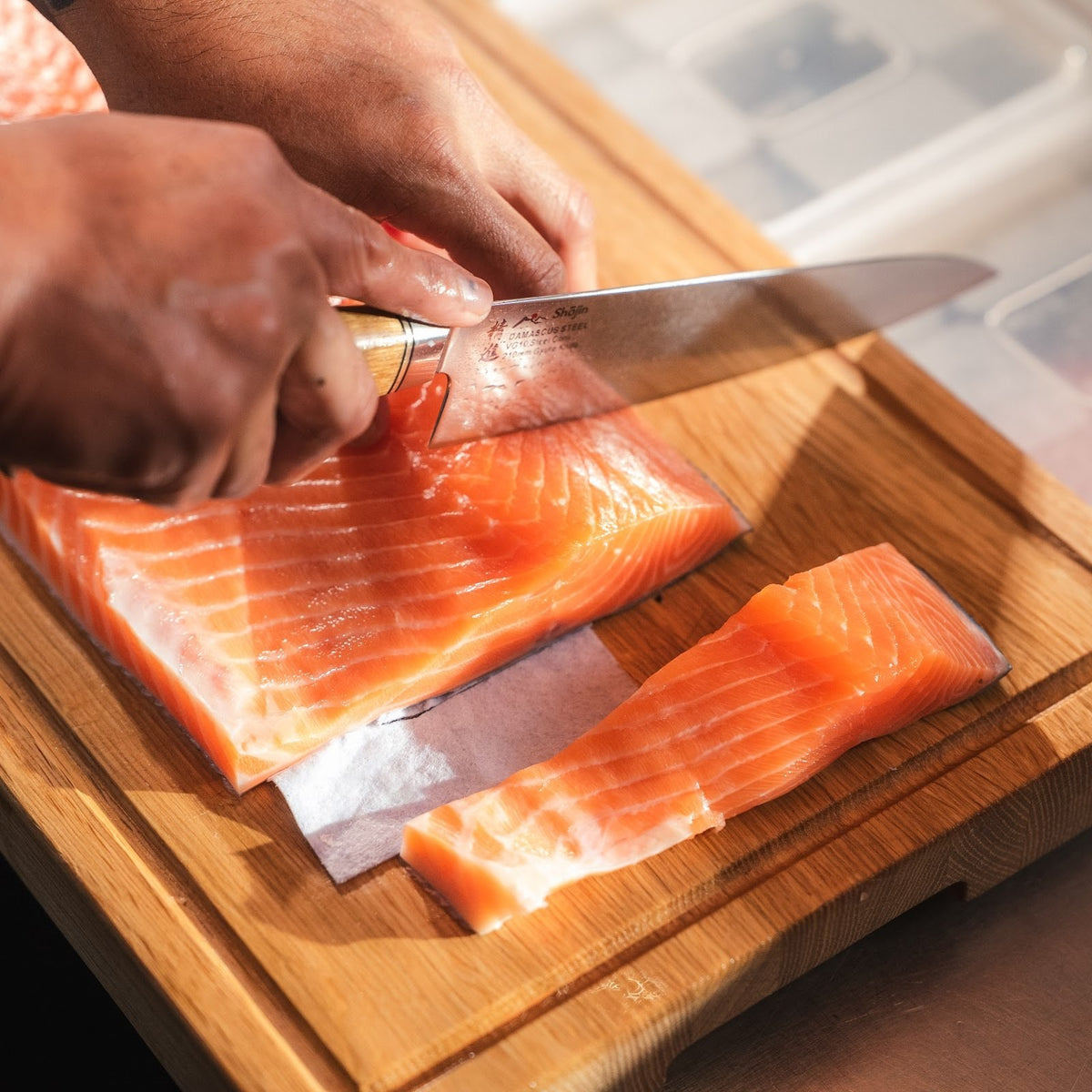 Lachs wird mit einem Shōjin Kaku Gyuto mit Eichengriff auf einem Schneidebrett aus Eiche portioniert