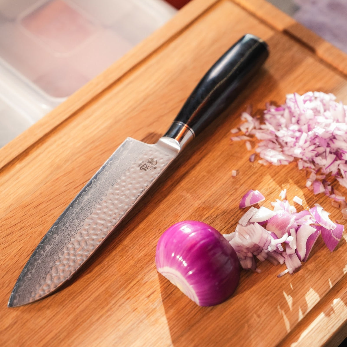 Shōjin Taru Santokumesser neben gehackter roter Zwiebel auf einem Schneidebrett aus Eiche