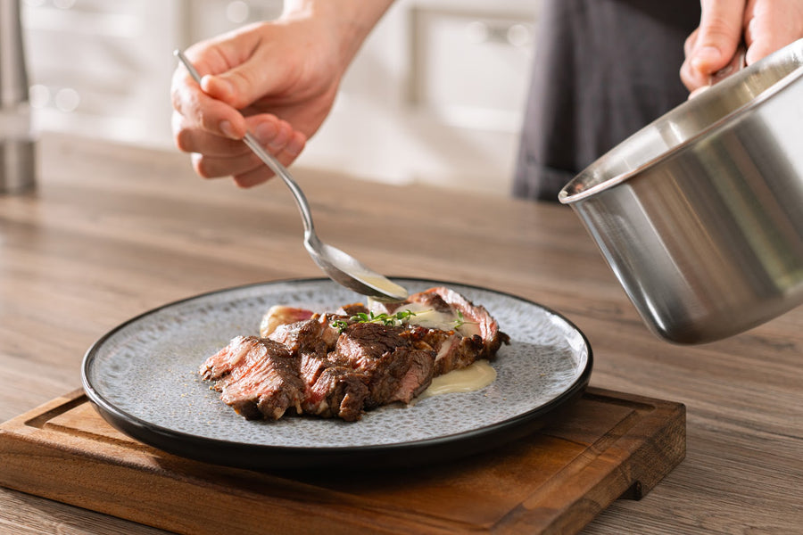 Soße wird aus einer Kasserolle über Steakscheiben gegossen