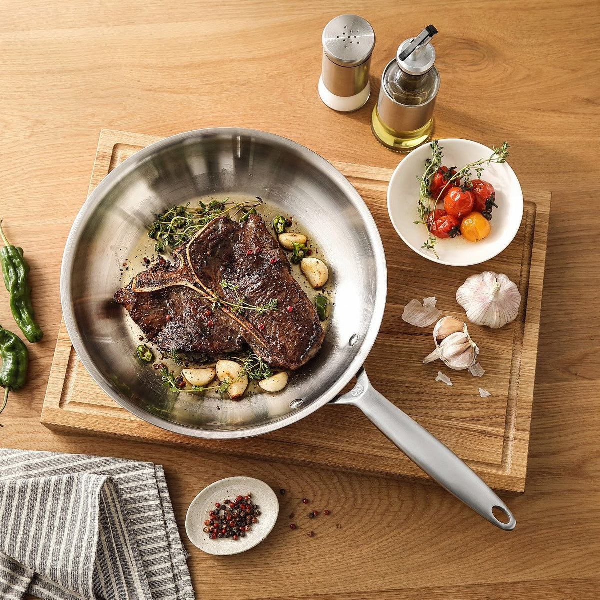 T-Bone-Steak mit Knoblauch in einer Bratpfanne aus 3-Ply Edelstahl auf einem Schneidebrett