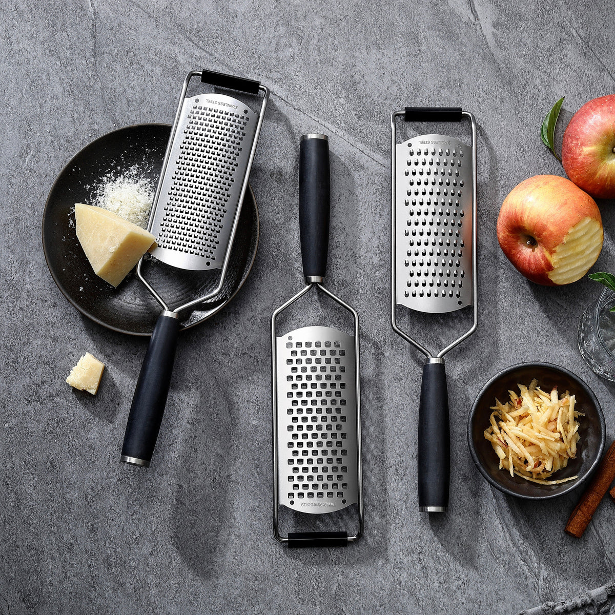 Die drei Reiben des Sets – fein, mittel und grob – mit Griffen aus G-10 neben Parmesan und Äpfeln