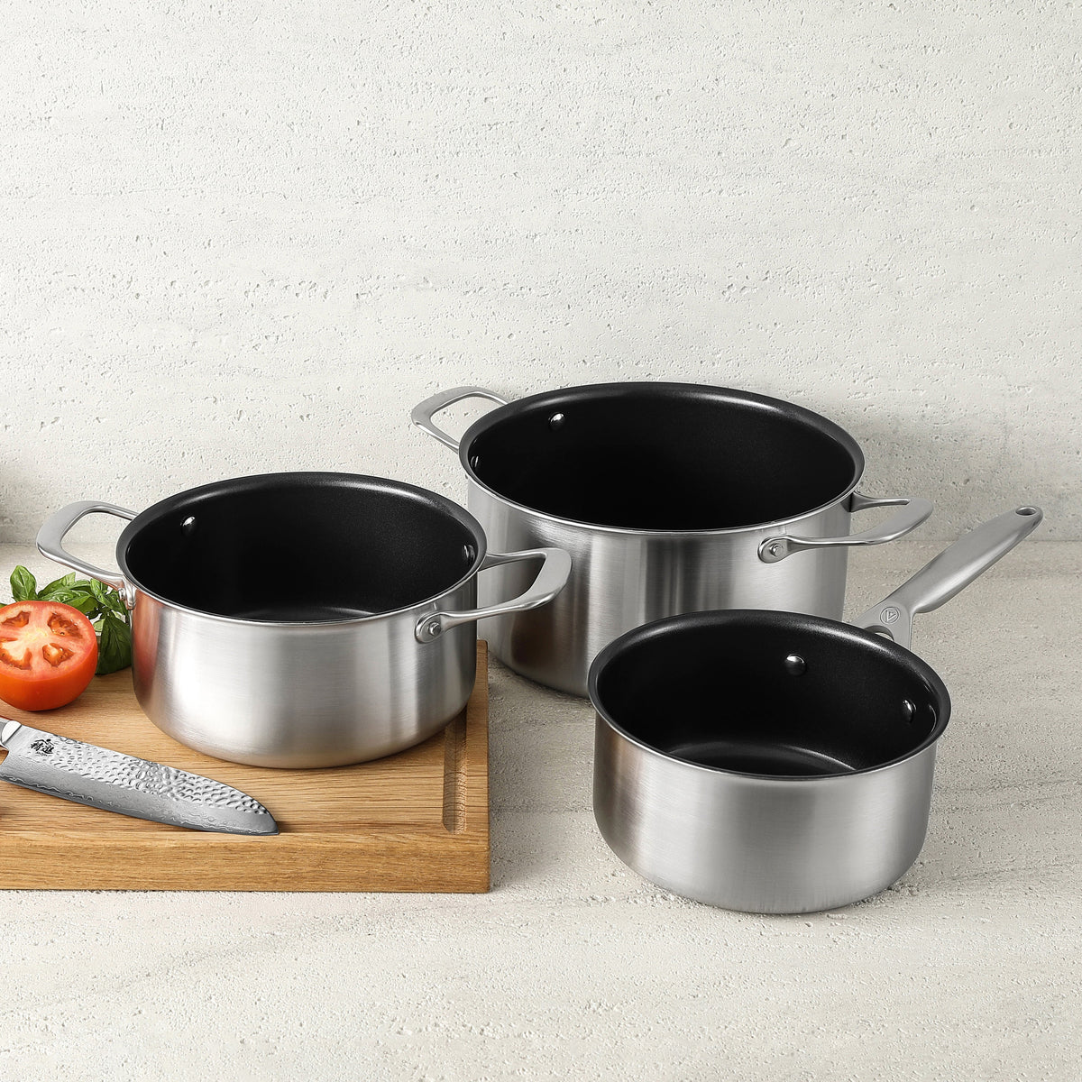 Kasserolle und Kochtöpfe 3-ply Keramik nebeneinander auf hellem Stein und einem Schneidebrett #Set_Kochtopf-Trio-Set - 3-teilig #Set_Signature-Set - 6-teilig #Set_Chef-Set - 7-teilig
