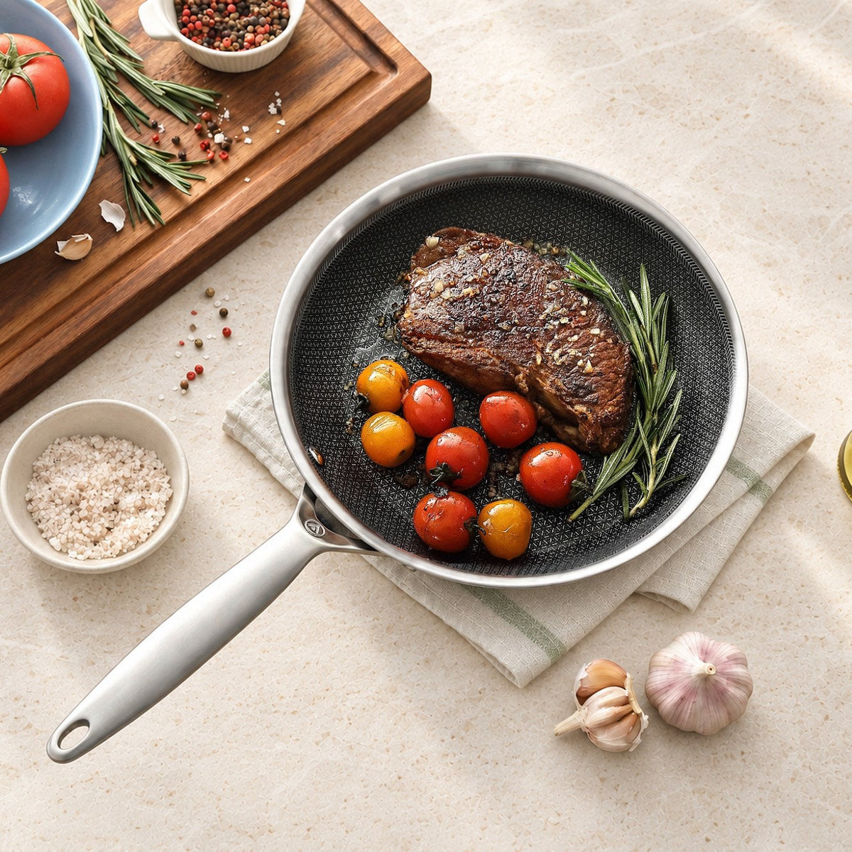 Steak mit Kirschtomaten und Rosmarin in einer Bratpfanne aus 3-Ply Hybrid auf hellem Stein, von oben