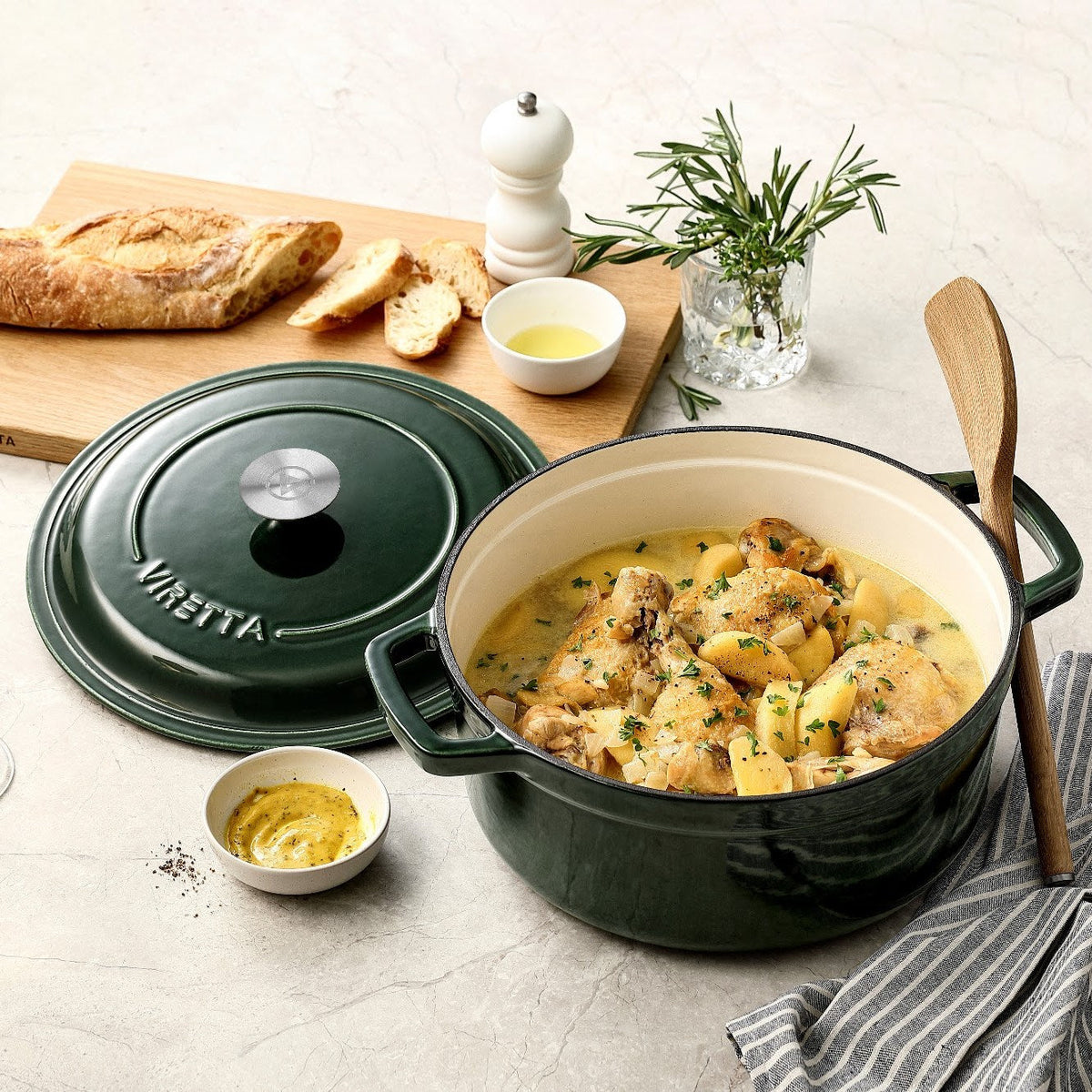 Moosgrüner Gusseisentopf mit Hähnchen und Kartoffeln, daneben der Deckel