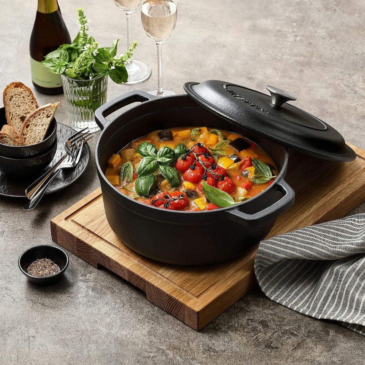 Schieferschwarzer Gusseisentopf mit Ratatouille und schräg aufgelegtem Deckel, auf einem Schneidebrett #Farbe_Schieferschwarz
