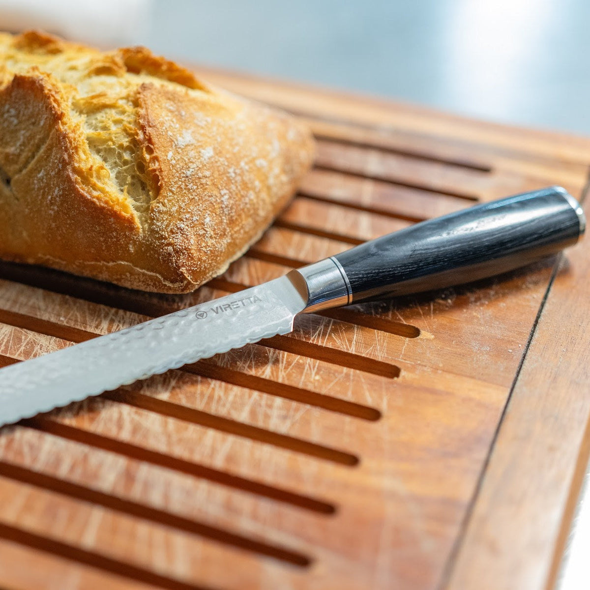 Shōjin Taru Brotmesser mit gehämmerter Oberfläche neben einem Sauerteigbrot auf einem Brotbrett
