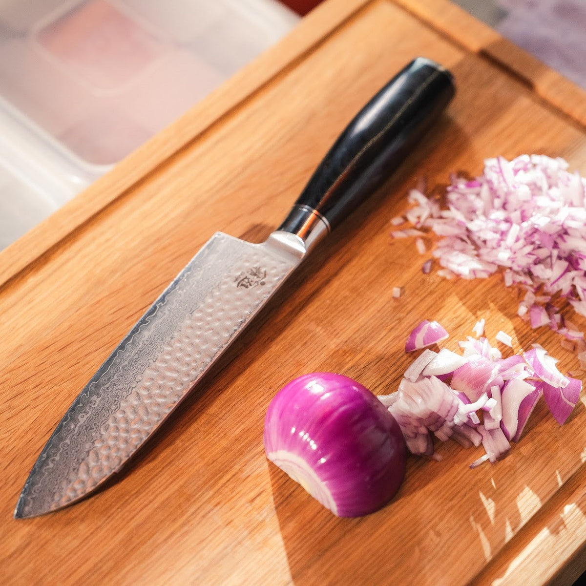 Shōjin Taru Santokumesser neben gehackter roter Zwiebel auf einem Schneidebrett aus Eiche
