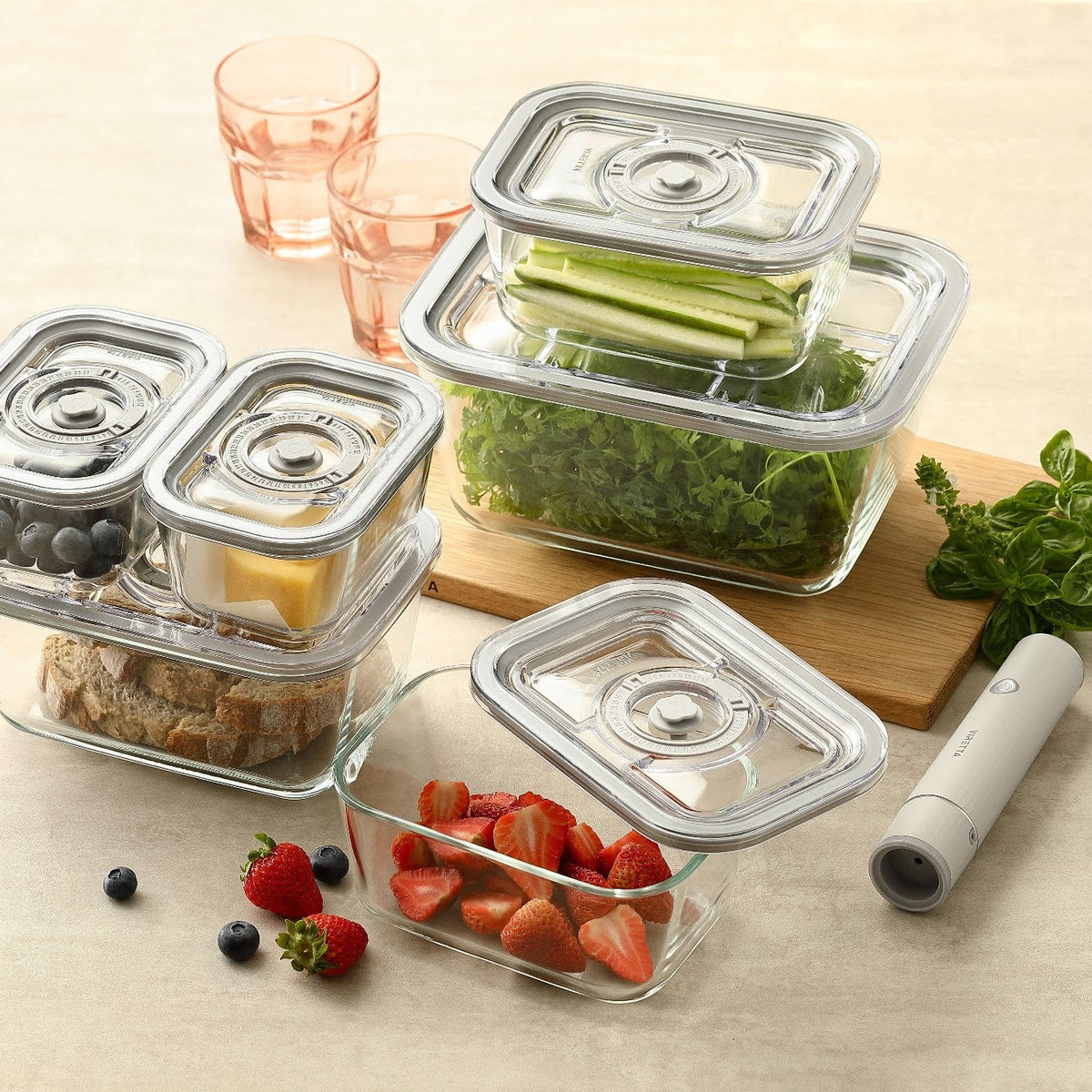 Vakuumbehälter aus Glas mit Beeren, Käse, Brot und Gemüse neben der elektrischen Vakuumpumpe