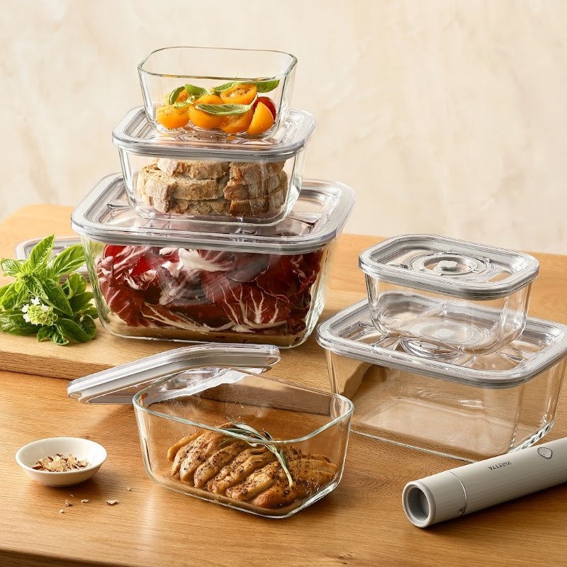 Vakuumbehälter aus Glas mit Tomaten, Brot, Salat und Hähnchen auf einem Esstisch
