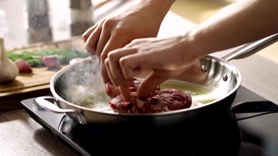 Ein Steak wird in eine 5-Ply-Pfanne aus Edelstahl gelegt und mit Butter arrosiert