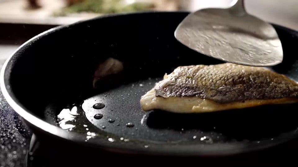 Ein Stück Fisch wird in eine Pfanne mit Titanium Plasma gelegt und mit einem Pfannenwender aus Metall gewendet