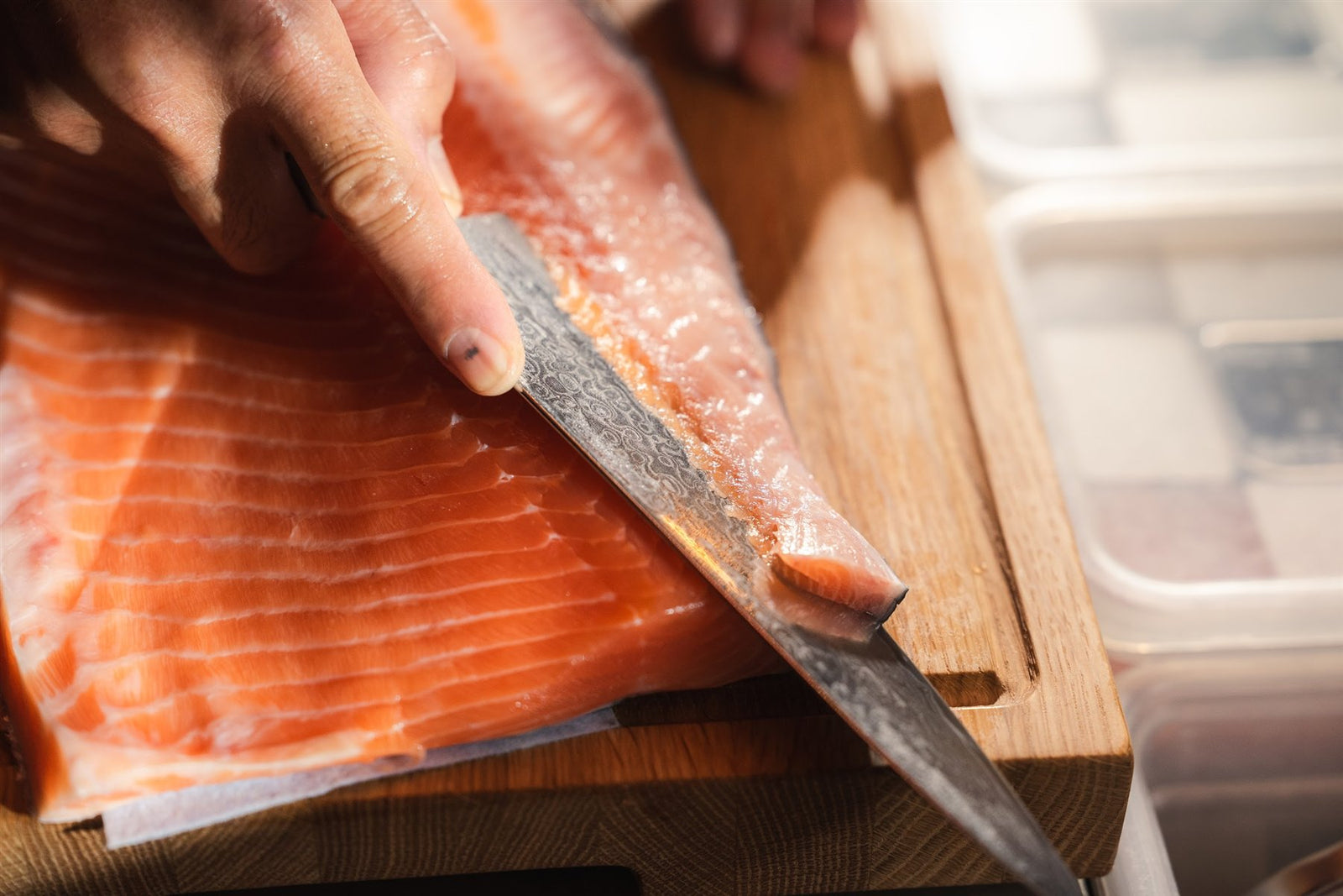 Die Klinge eines Shōjin Kaku Gyutos schneidet Lachs auf einem Holzbrett
